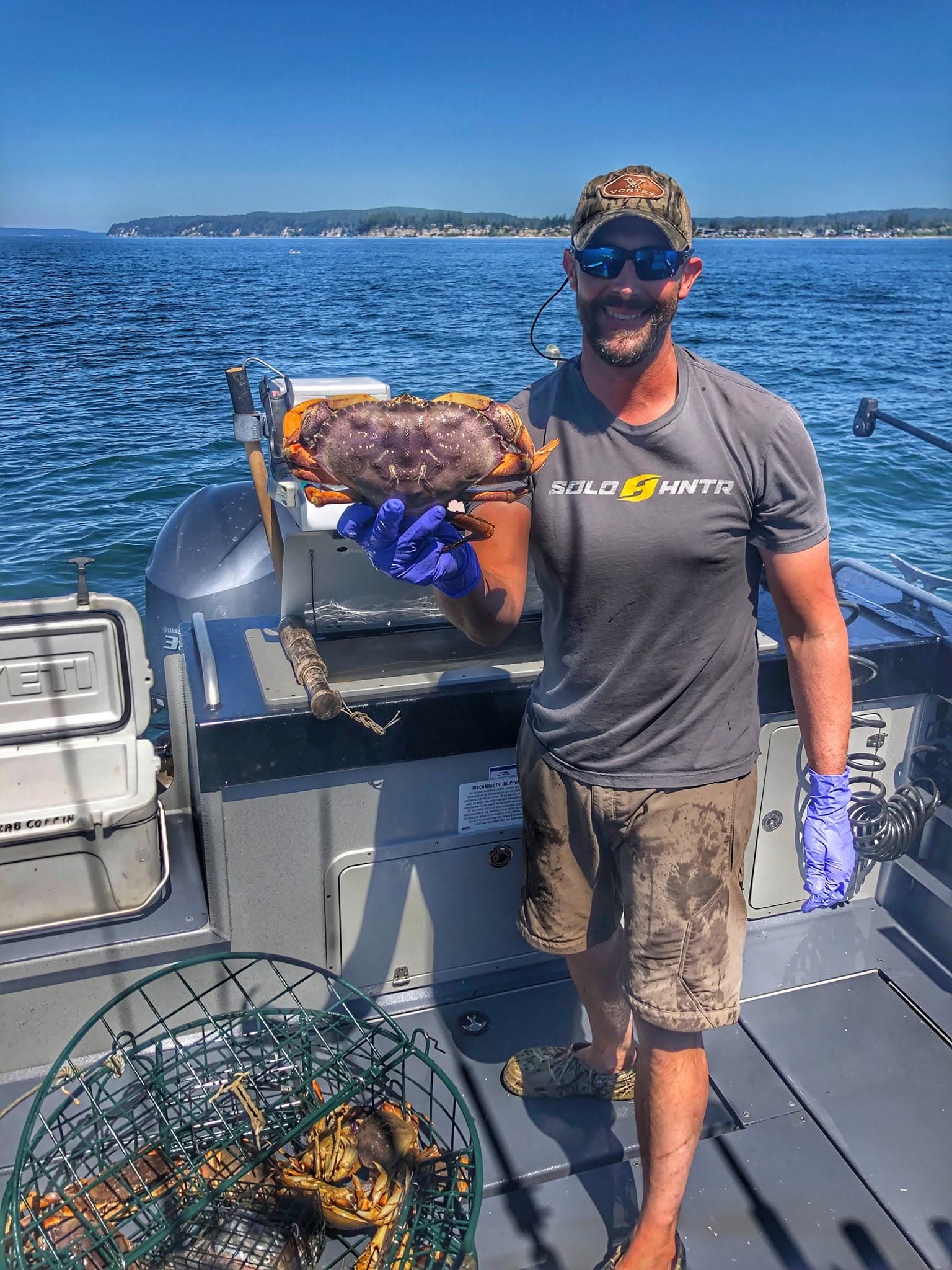 An angler on a Puget Sound boat holding up a Dungeness crab beside a crab pot